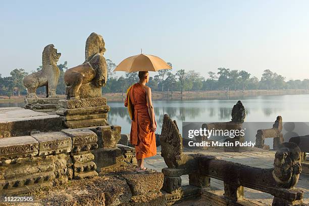 buddhist monk standing next to stone carvings - kambodscha stock-fotos und bilder