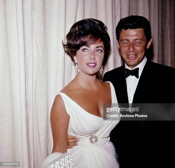 Elizabeth Taylor and Eddie Fisher attending an event, circa 195=60. Taylor wears a white dress, with a brooch at the waist.