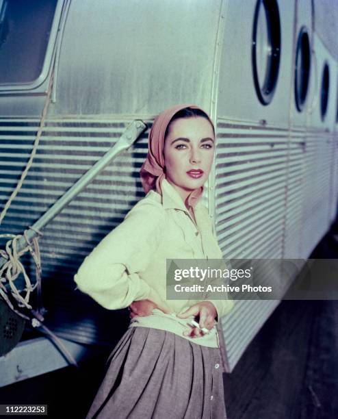 Elizabeth Taylor leaning against a dressing room trailer while smoking a cigarette on the set of director George Stevens's 1956 film, 'Giant'.