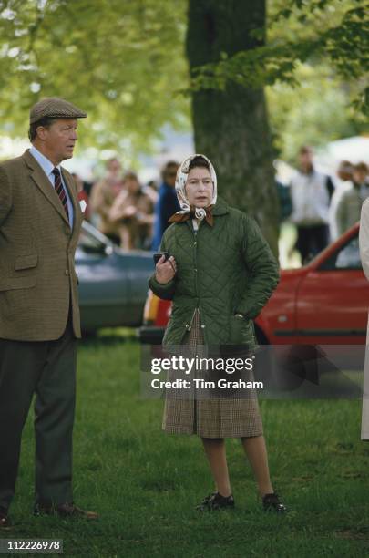 Queen Elizabeth II, wearing a headscarf, and Sir Michael Oswald, manager of the Royal Stud, attending the Royal Windsor Horse Show, held at Home Park...