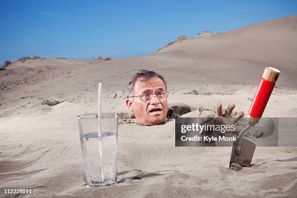 caucasian man buried in sand next to glass of water and trowel - buried in sand stockfoto's en -beelden