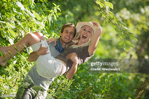 man carrying woman in forest, smiling - bermuda shorts stock pictures, royalty-free photos & images