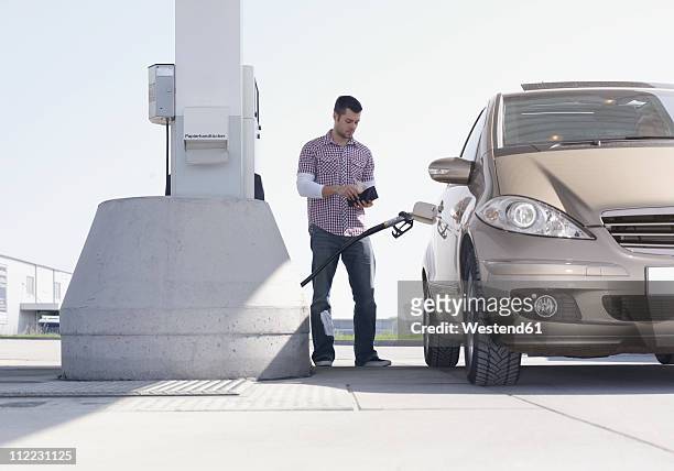 germany, augsburg, young man at petrol pump with car - refueling photos et images de collection