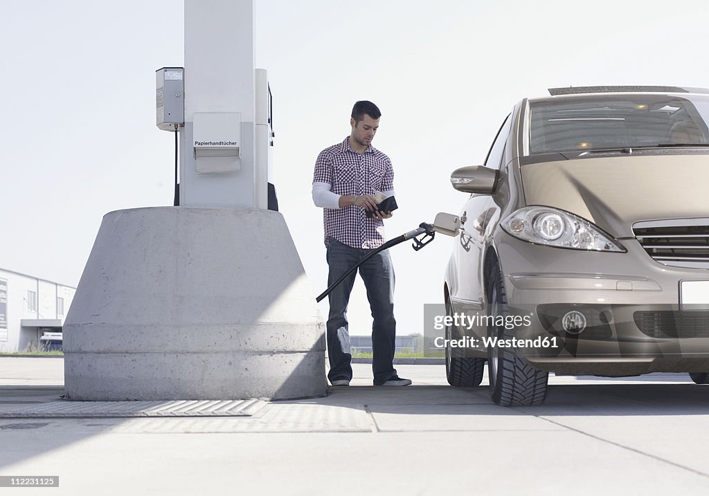 Germany, Augsburg, Young man at petrol pump with car