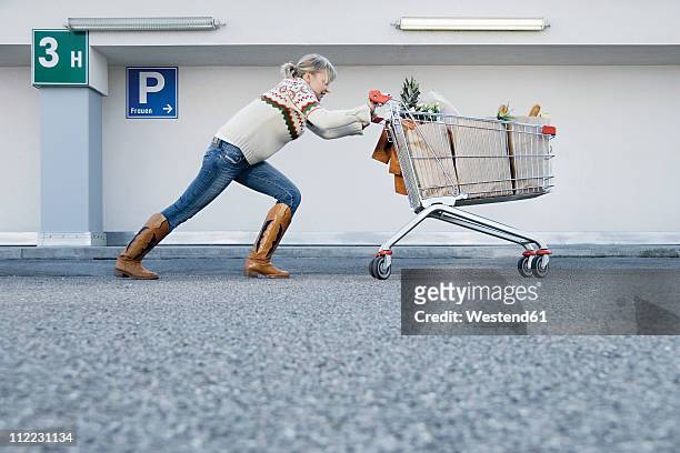 germany, young woman pushing shopping cart - empujar fotografías e imágenes de stock