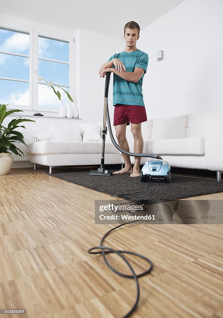 Germany, Augsburg, Man cleaning apartment with vacuum cleaner