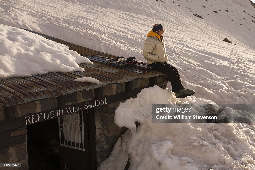 A woman sitting on the roof of a mountain climbers hut buried by snow on Volcan San Jose in the Andes mountains of Chile