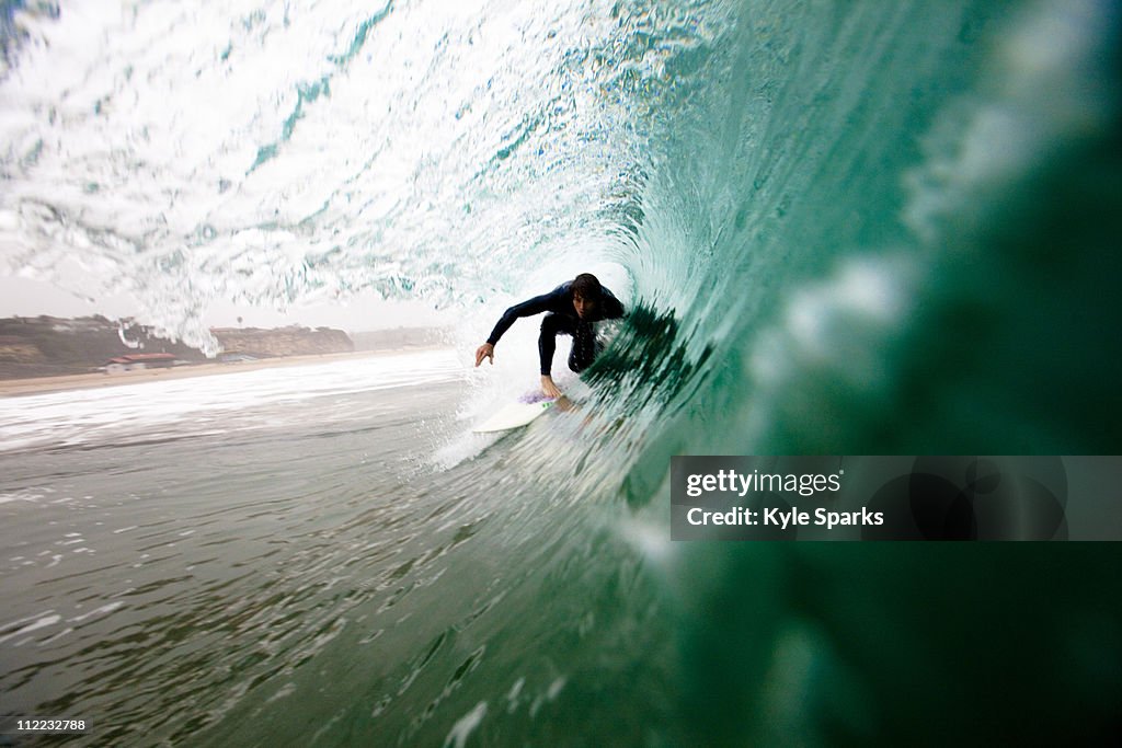 A male surfer pulls into a barrel while surfing at Zuma beach in Malibu, California.