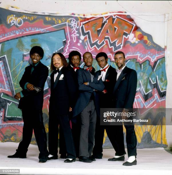 Portrait of Grandmaster Flash and the Furious Five, formally dressed, and standing in front of graffiti painted cloth tacked up against the studio...