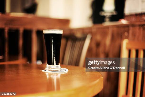 glass of guinness on pub table - irish pub fotografías e imágenes de stock