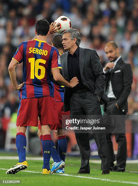 Sergio Busquets of Barcelona holds head coach Jose Mourinho of Real Madrid by his shirt as they chat while head coach Josep Guardiola of Barcelona...