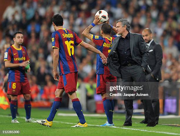 Sergio Busquets of Barcelona holds head coach Jose Mourinho of Real Madrid by his shirt as they chat while head coach Josep Guardiola of Barcelona...