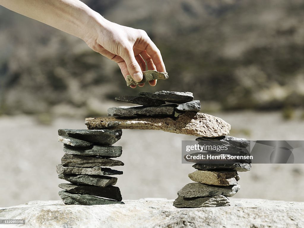 Hand placing stone on balancing rock bridge
