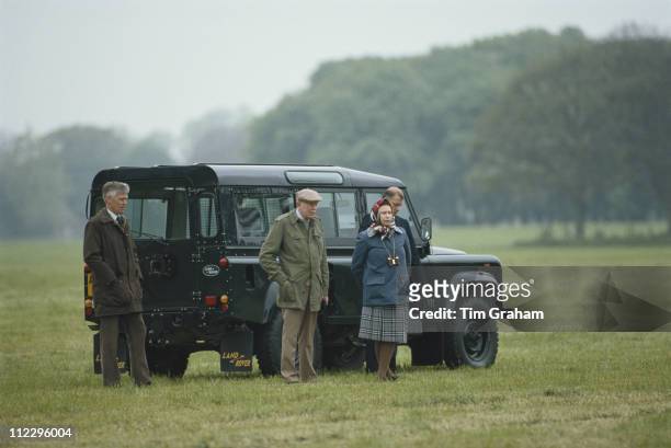 Queen Elizabeth II with Crown Equerry Lt Col Sir John Miller as well as her bodyguard and chauffeur, standing by a Land Rover on the Windsor estate...