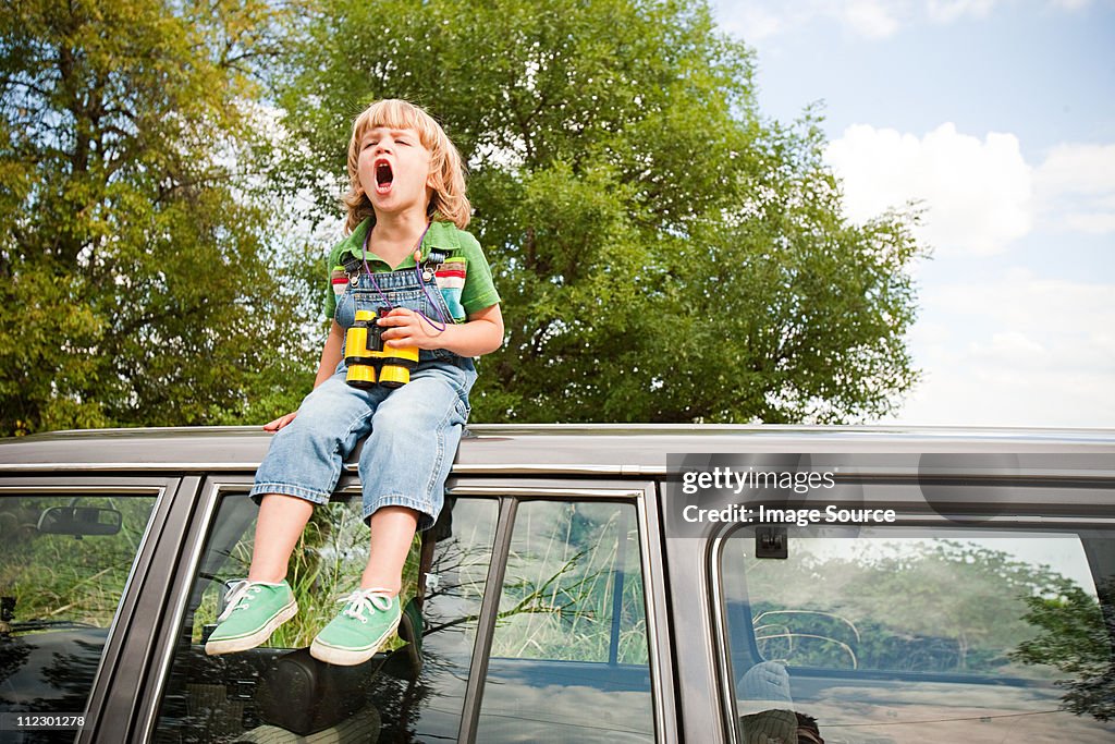 Boy with binoculars, sitting on roof of car