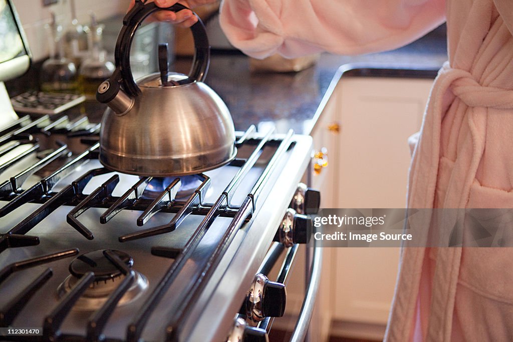 Mujer ebullición tetera en hob PARA HACER TÉ