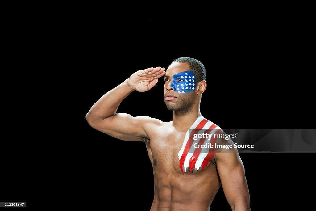 Man with US flag painted on face and shoulder saluting