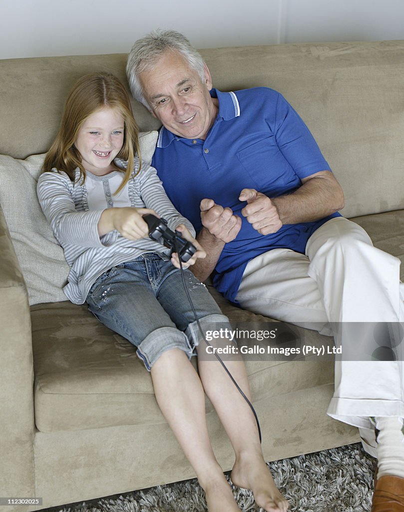 Young girl playing video games with grandfather on the couch, Bakoven, Western Cape Province, South Africa