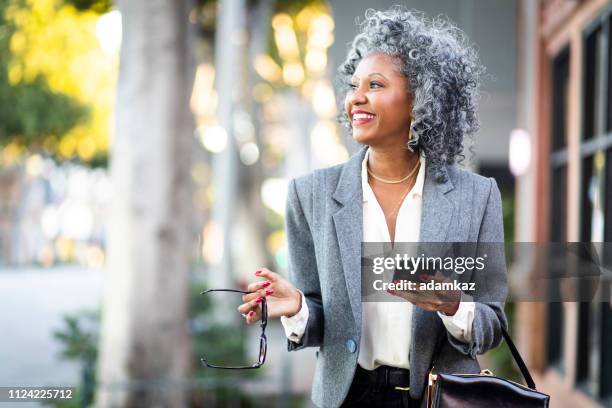 mature black woman texting while walking in city - older black people shopping stock pictures, royalty-free photos & images