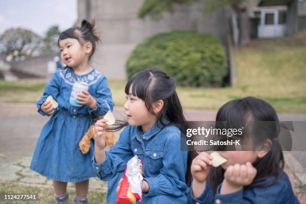 three little sisters eating snack in public park - family eating potato chips stock pictures, royalty-free photos & images