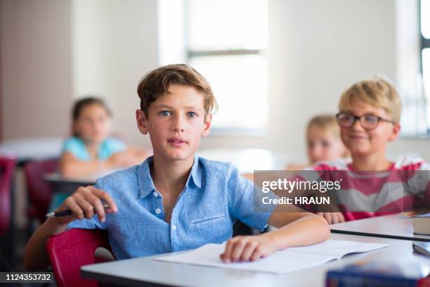 schoolboy sitting with friends in classroom - junior stock pictures, royalty-free photos & images