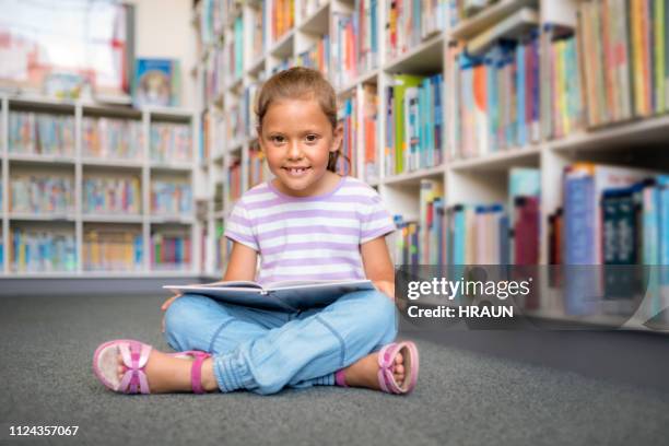 cute girl reading book in school library - cross legged stock pictures, royalty-free photos & images