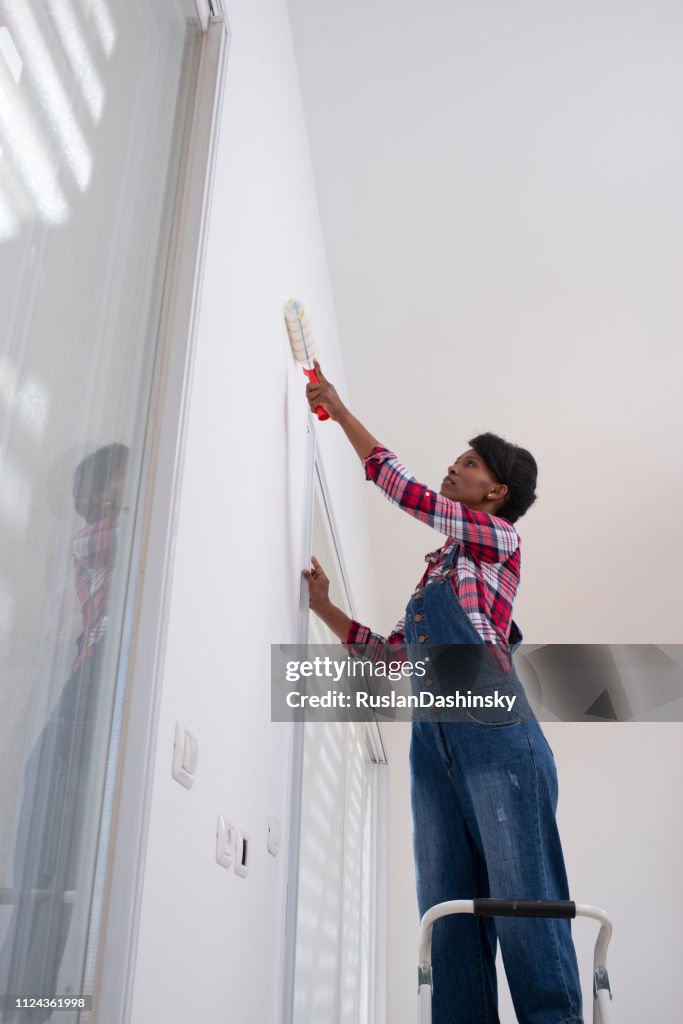 Interior house painting. Woman painting living room wall with paint roller.