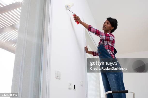 interior house painting. woman painting living room wall with paint roller. - service level high stock pictures, royalty-free photos & images