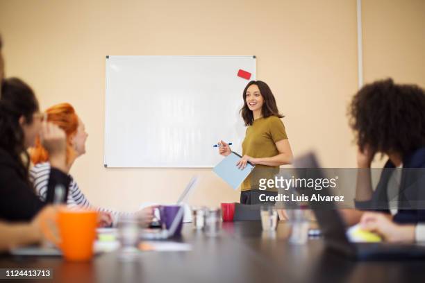businesswoman addressing colleagues at a meeting - präsentieren whiteboard stock-fotos und bilder