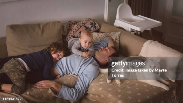 dad, two babies and a cat laying in the sofa - crowded home stock-fotos und bilder