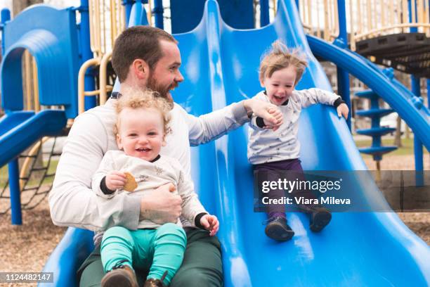 father and sons playing on slide - playground equipment stock pictures, royalty-free photos & images