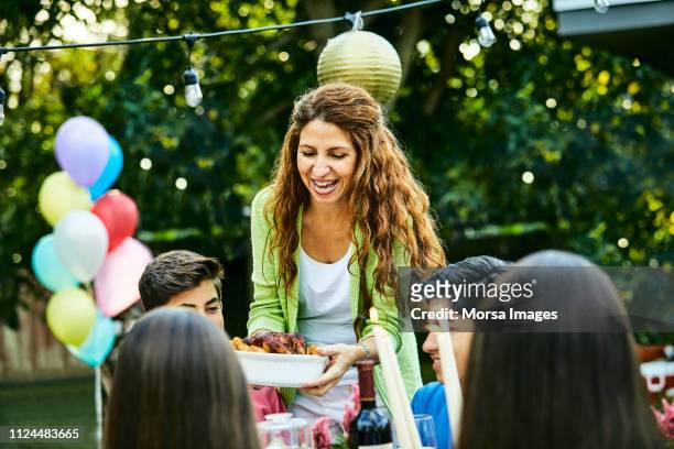 cheerful mature woman serving food to kids - boy party photos et images de collection