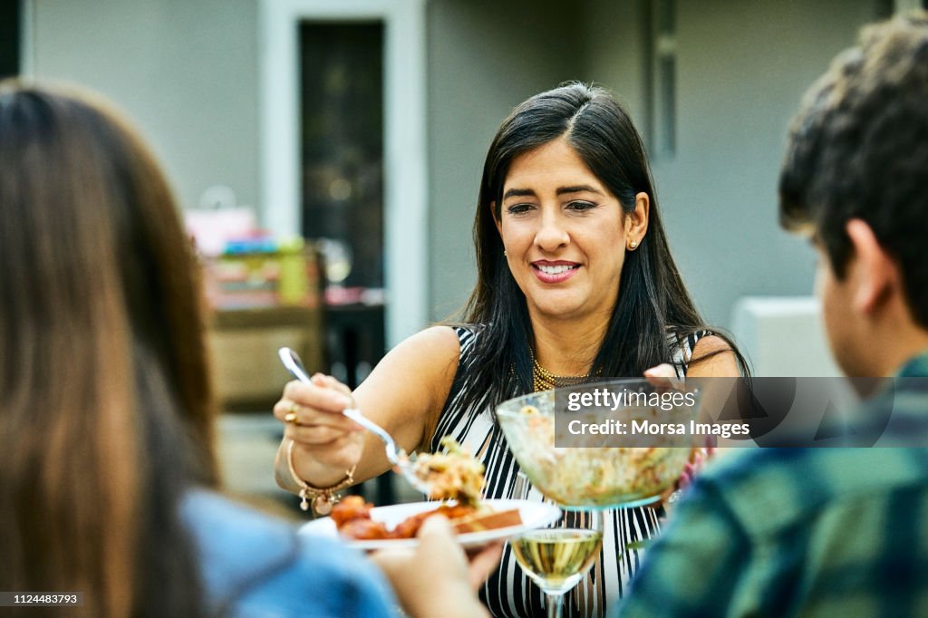Smiling woman serving food to teenagers at table