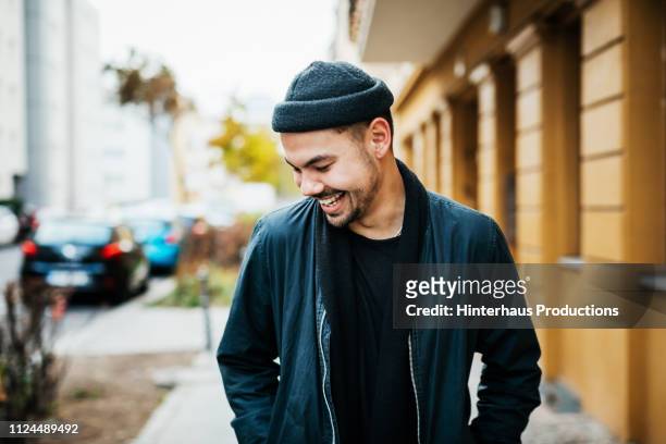 stylish young man laughing in city street - wollmütze stock-fotos und bilder