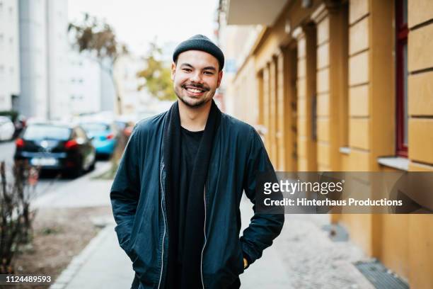 portrait of young man smiling in city street - leben in der stadt stock-fotos und bilder