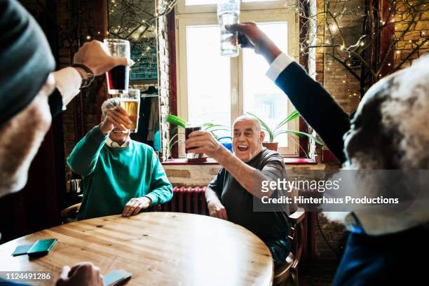 older group of friends toasting each other at bar - round table stockfoto's en -beelden