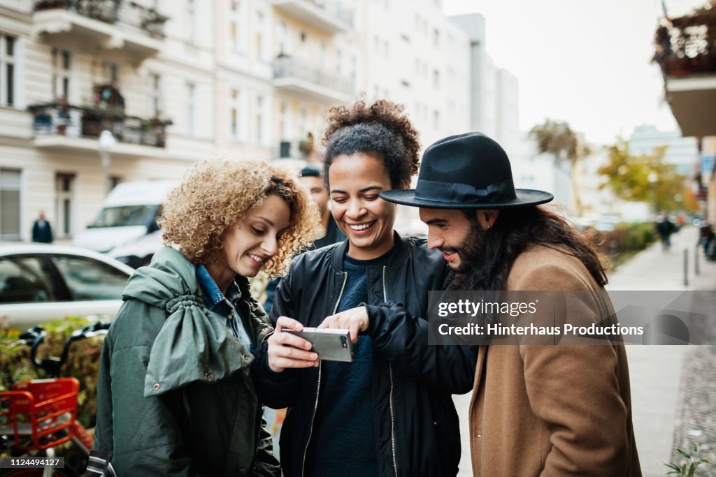 Group Of Friends Looking At Smartphone In Street