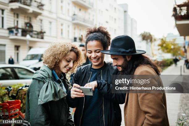 group of friends looking at smartphone in street - movilidad urbana fotografías e imágenes de stock