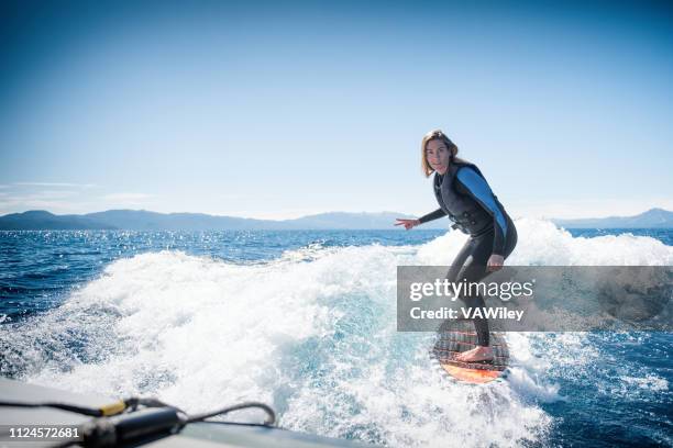 strong, independent woman wake surfing behind a boat in lake tahoe. - woman surfing stock pictures, royalty-free photos & images
