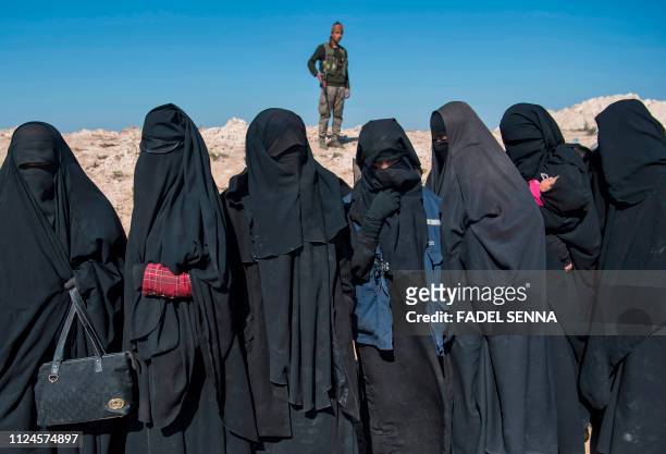Fighter with the US-backed Syrian Democratic Forces keeps watch near veiled women standing on a field after they fled from the Baghouz area in the...