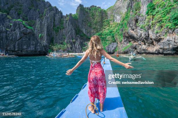 vrolijke jonge vrouw armen wijd open op vissersboot varen tropische lagunes - inviting gesture stockfoto's en -beelden