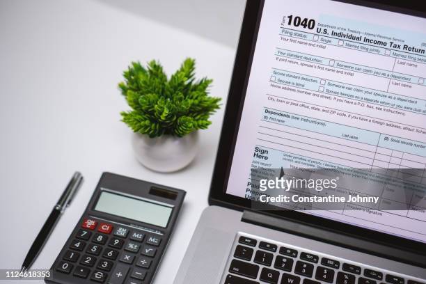 tax form on laptop screen on work desk with pen and calculator - 2019 taxes stock pictures, royalty-free photos & images