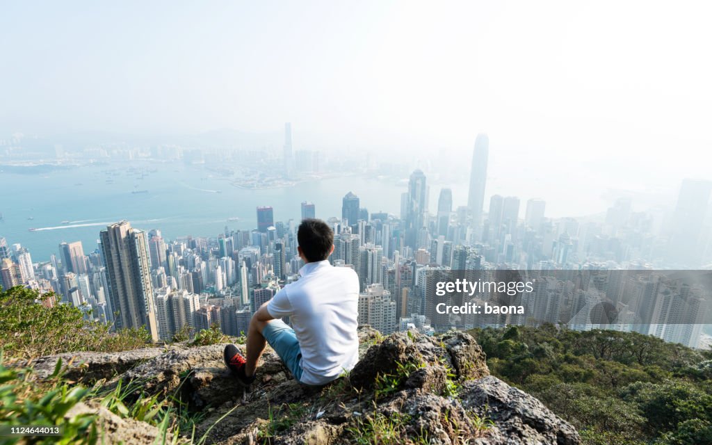 Men sitting on the top of mountain and looking cityscape