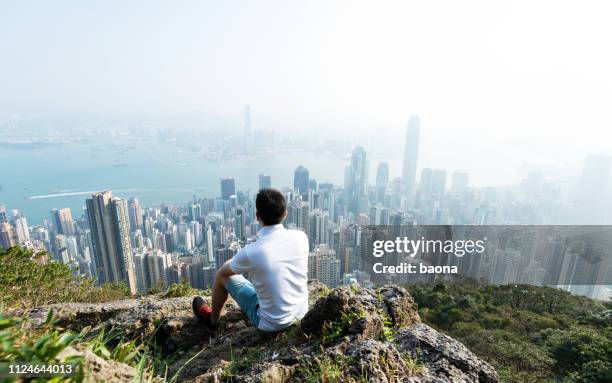 男人坐在山頂上, 看著城市景觀 - 在頂部 個照片及圖片檔