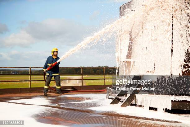 firemen training, fireman spraying firefighting foam at training facility - esferovite imagens e fotografias de stock