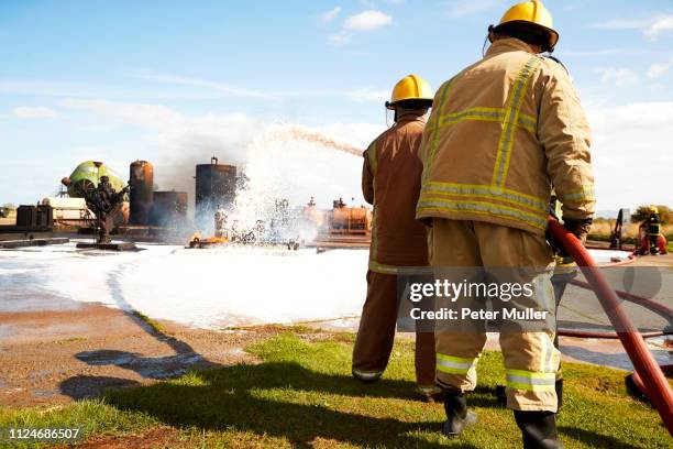 firemen training, team of firemen spraying firefighting foam at training facility - international firefighters day stock pictures, royalty-free photos & images