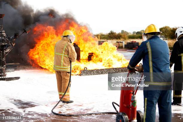 firemen training, team of firemen spraying firefighting foam on fire at training facility, rear view - international firefighters day stock pictures, royalty-free photos & images