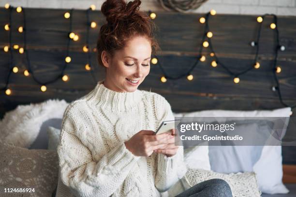 woman texting on bed decorated with christmas lights - daily life during christmas season in poland foto e immagini stock
