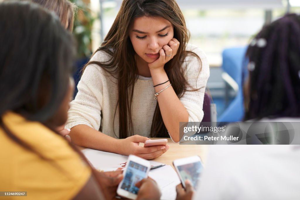 Female higher education students looking at smartphones in college classroom