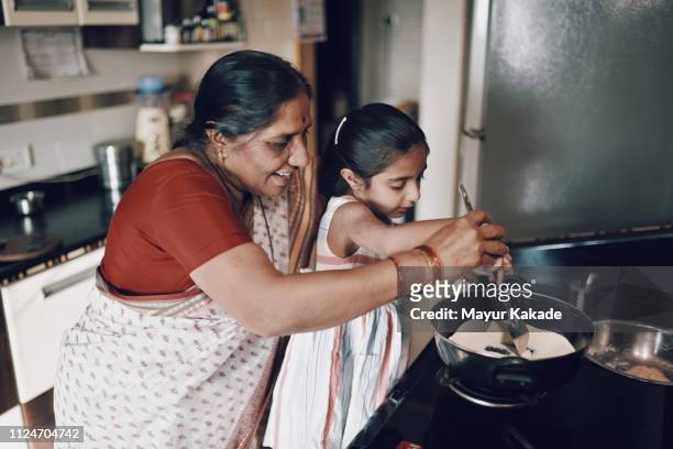 young girl helping her grandmother while working in the kitchen - daily life in india stockfoto's en -beelden
